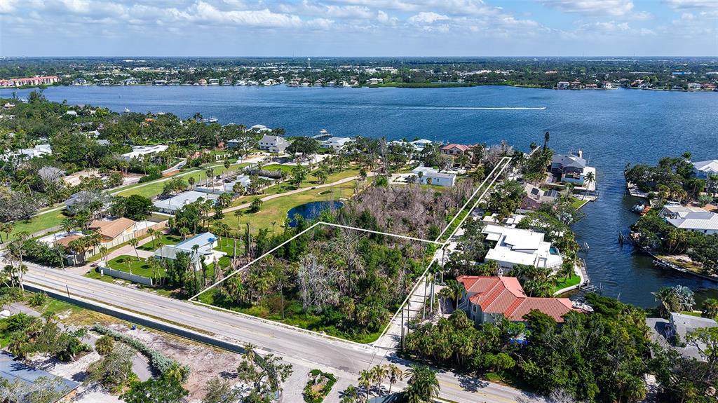 An aerial view shows a vacant, wooded lot outlined in white near a waterfront neighborhood — 7401-A MIDNIGHT PASS ROAD UNIT A, SARASOTA, FL
