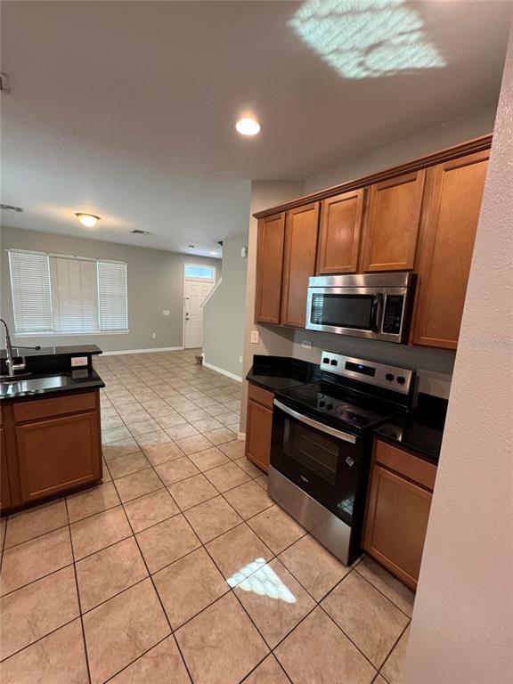 A kitchen with wood cabinets, black countertops, and stainless steel appliances overlooks an open living area — 11938 SILVERLAKE PARK DRIVE, WINDERMERE, FL