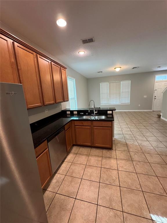 A kitchen with wood cabinets, black countertops, and tile flooring opens into a living area — 11938 SILVERLAKE PARK DRIVE, WINDERMERE, FL