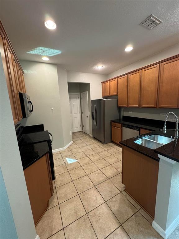 A kitchen features wood cabinets, black countertops, stainless steel appliances, and light-colored tile flooring — 11938 SILVERLAKE PARK DRIVE, WINDERMERE, FL