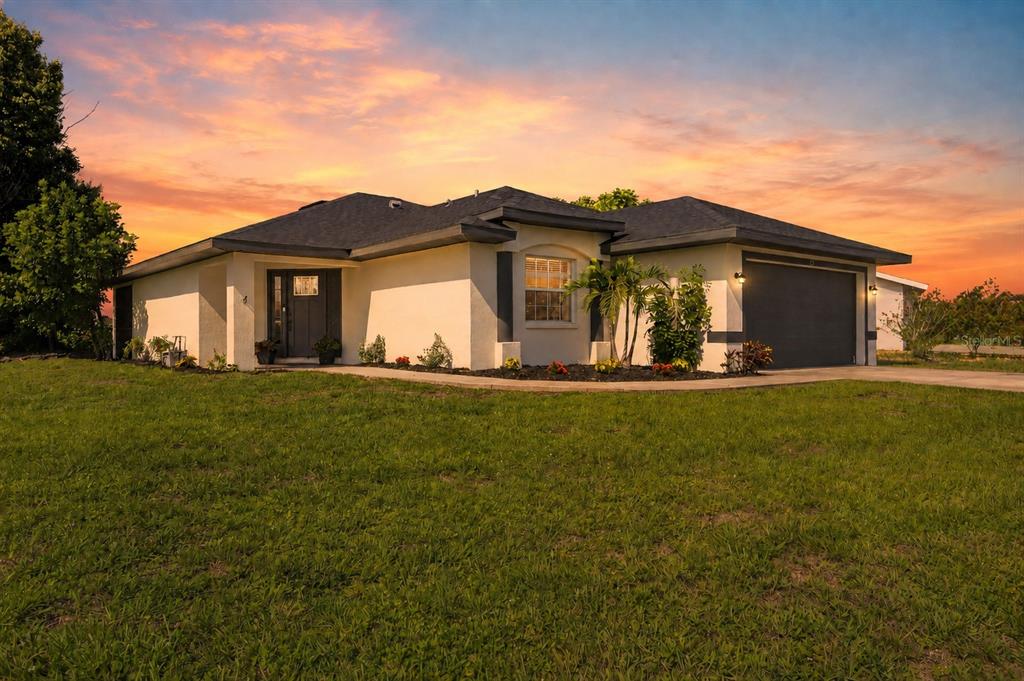 A single-story house with a dark garage door and a front entrance at sunset — 23 BUNKER PLACE, ROTONDA WEST, FL