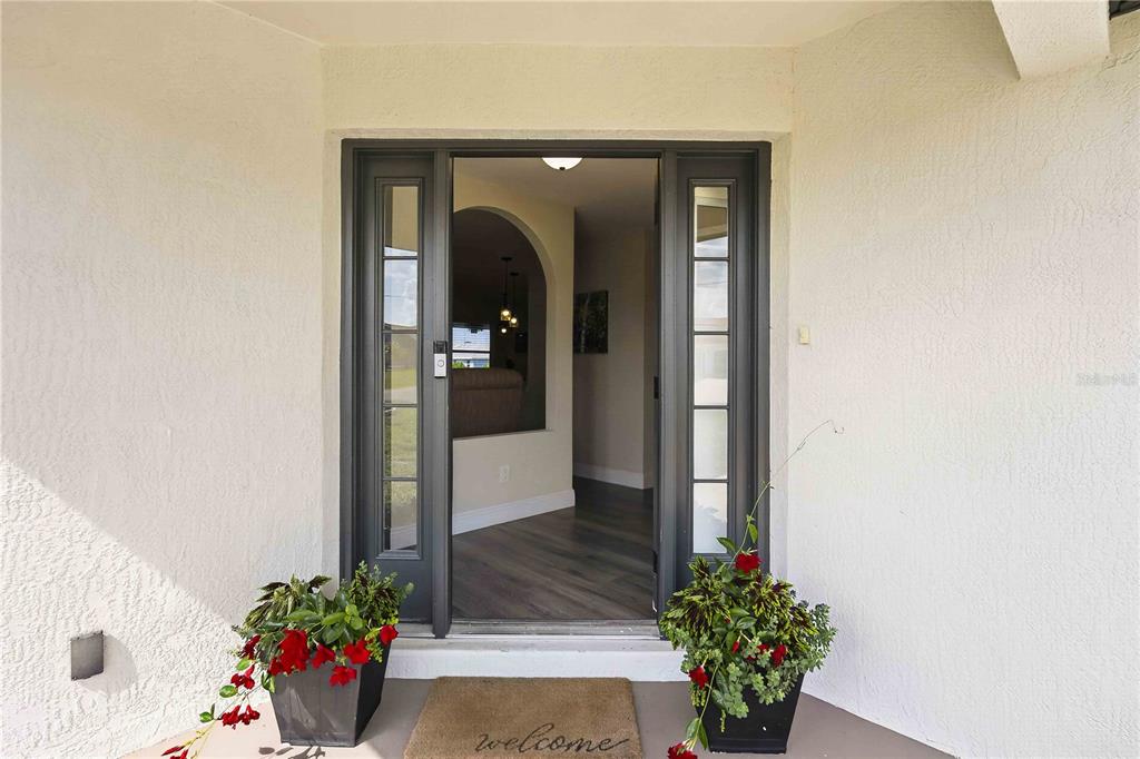 A front entryway with a dark-framed glass door, a welcome mat, and two potted plants — 23 BUNKER PLACE, ROTONDA WEST, FL
