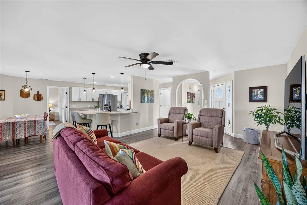 An open-concept living room and kitchen featuring wood-look flooring, a red sofa, and two armchairs — 23 BUNKER PLACE, ROTONDA WEST, FL