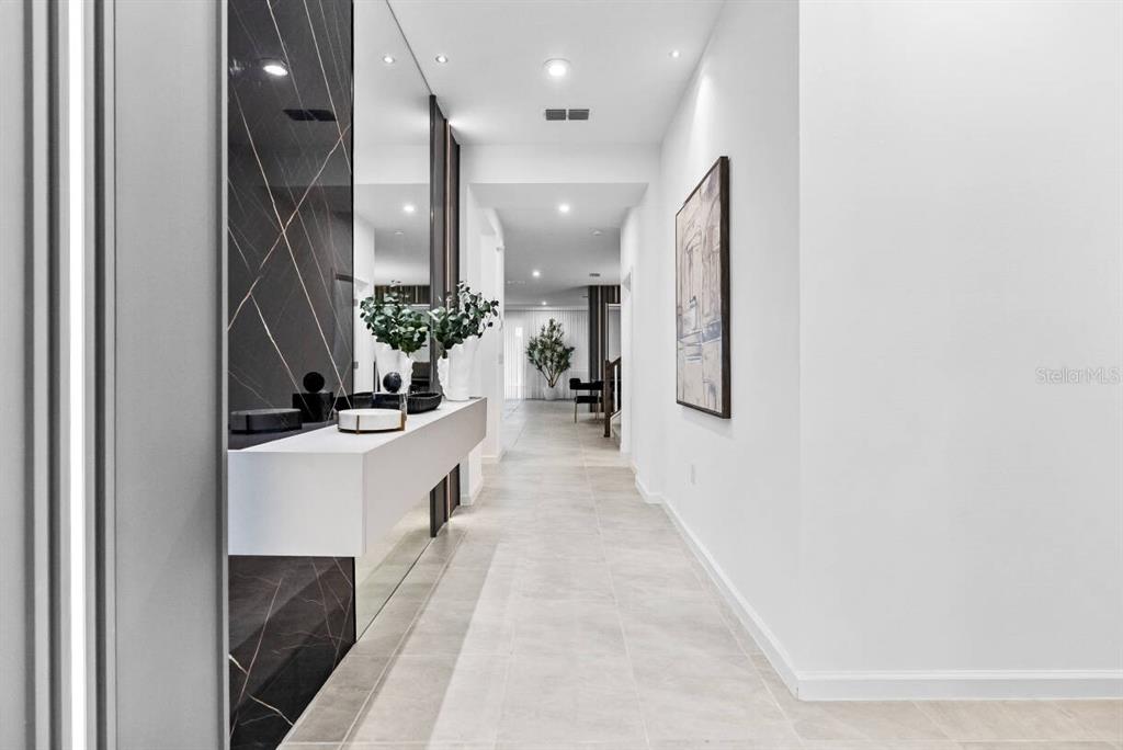A modern hallway features a floating white console table against a black marble accent wall — 9179 BREEZE MIST TERRACE, DAVENPORT, FL