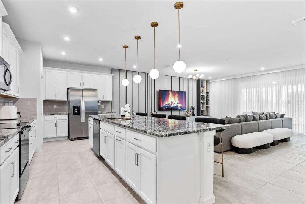 A modern kitchen with white cabinets, granite countertops, and a large island faces a living area — 9179 BREEZE MIST TERRACE, DAVENPORT, FL