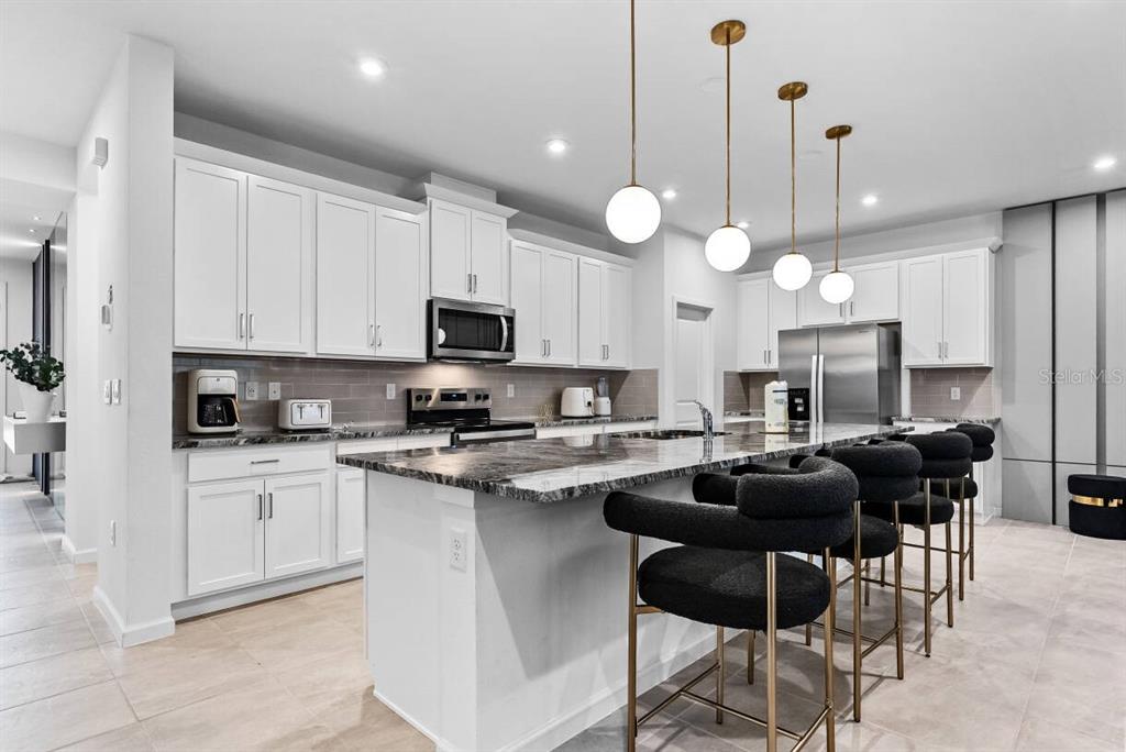 A modern kitchen features white cabinetry, a large marble island, and four black bar stools — 9179 BREEZE MIST TERRACE, DAVENPORT, FL