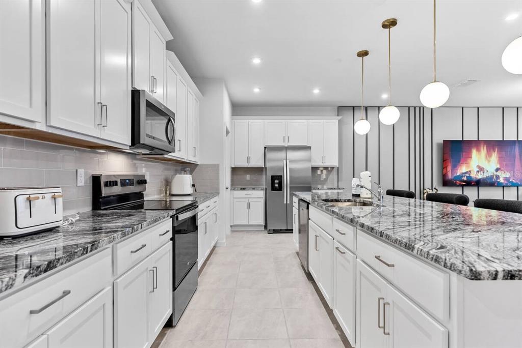A modern kitchen features white cabinets, granite countertops, stainless steel appliances, and a large island — 9179 BREEZE MIST TERRACE, DAVENPORT, FL