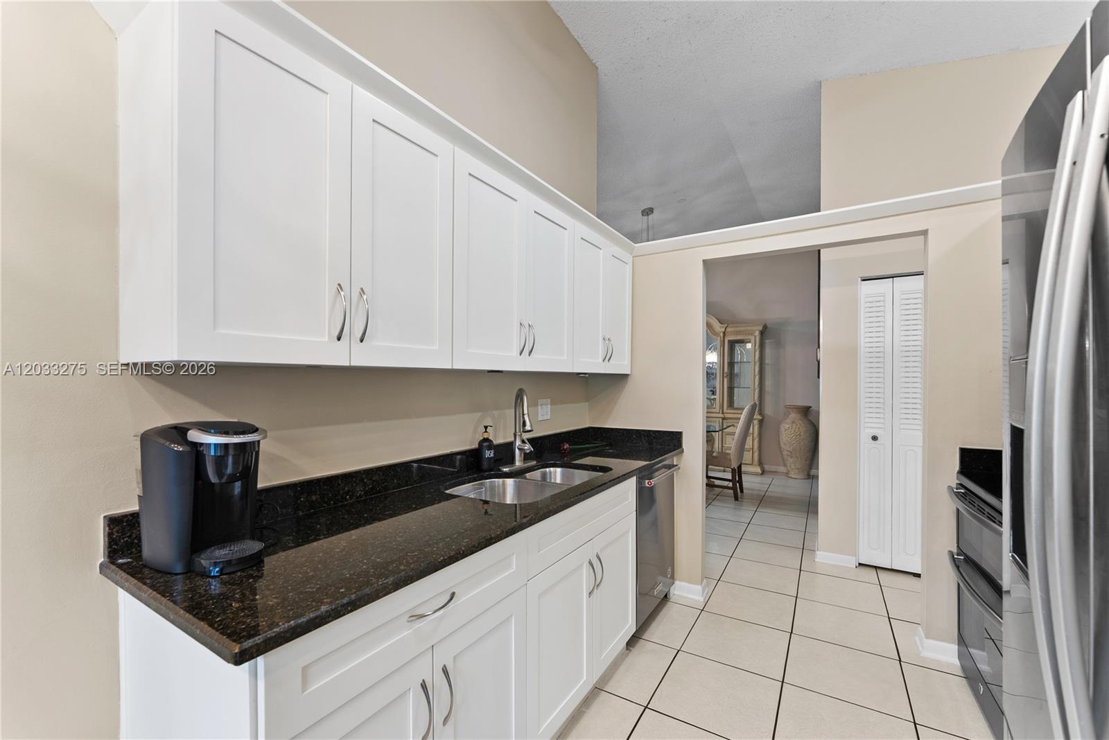 A kitchen features white cabinets, black granite countertops, a stainless steel sink, and tile flooring — 4148 N Palm Forest Dr N, Delray Beach FL 33445, DELRAY BEACH, FL