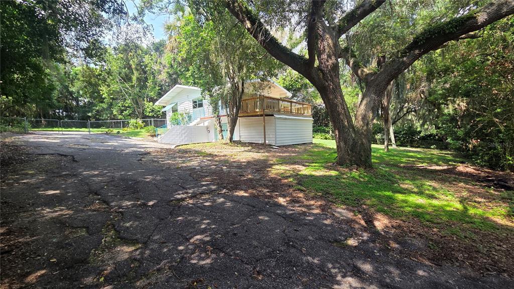 A white house with a wooden deck sits behind a large tree and cracked driveway — 205 CATHERINE AVENUE, BABSON PARK, FL