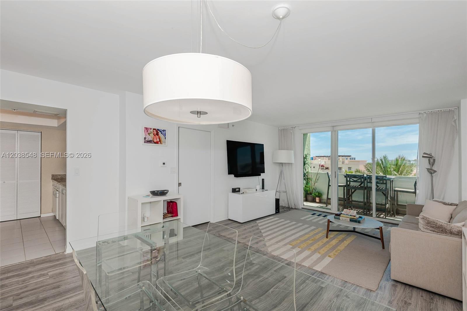 A living and dining area features a glass table, neutral sofa, and a balcony view — 90 Alton Rd # 607, Miami Beach FL 33139, MIAMI BEACH, FL
