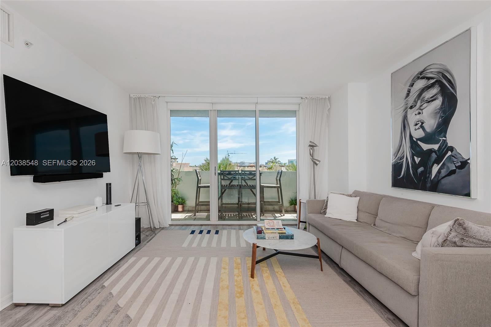 A living room features a grey sofa, a white media console, and a balcony view — 90 Alton Rd # 607, Miami Beach FL 33139, MIAMI BEACH, FL