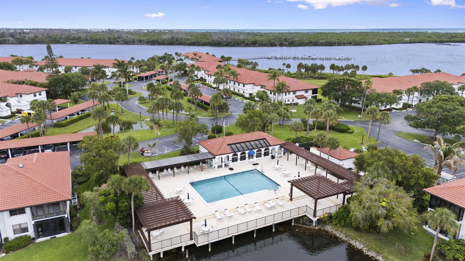 An aerial view shows a swimming pool deck with pergolas overlooking a bay and buildings — 6102 SE Landing Way # 14, Stuart FL 34997, STUART, FL