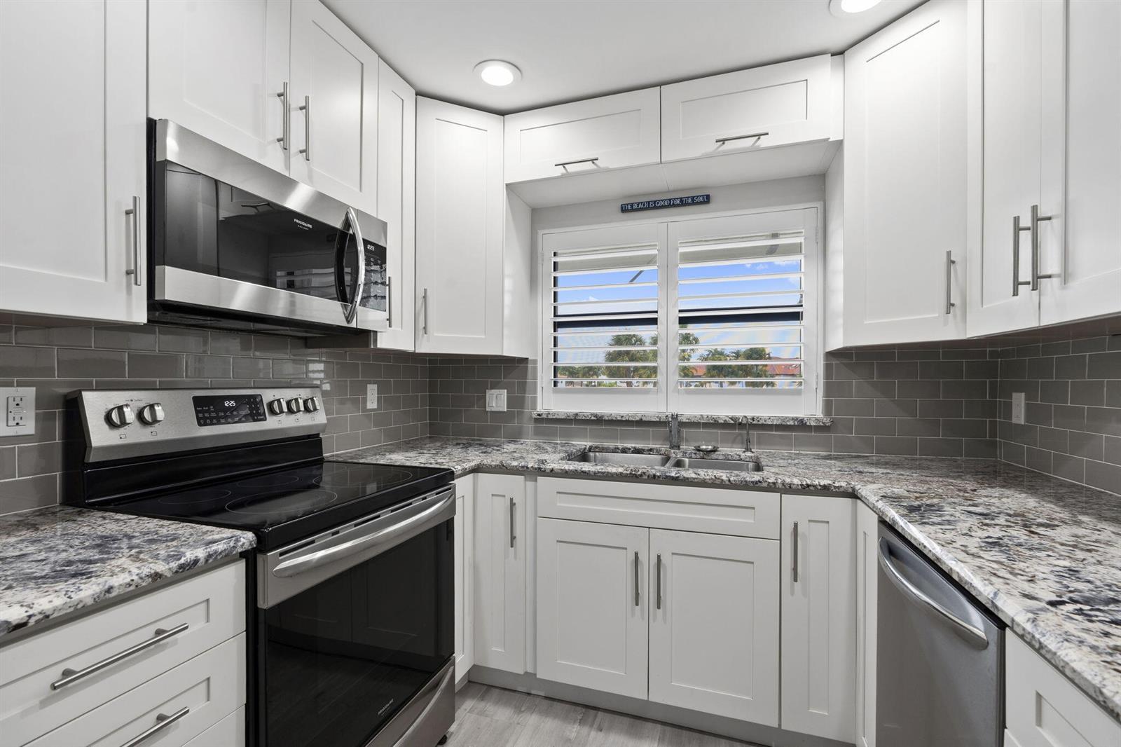 A kitchen with white cabinets, granite countertops, stainless steel appliances, and gray subway tile backsplash — 6102 SE Landing Way # 14, Stuart FL 34997, STUART, FL