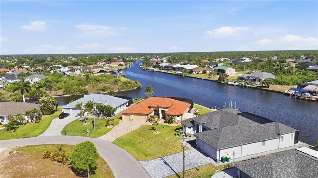 An aerial view shows waterfront houses with tiled and shingled roofs along a canal — 9266 MIGUE CIRCLE, PORT CHARLOTTE, FL