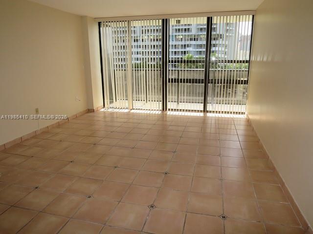 An empty room features light-colored tile flooring and a large sliding glass door with blinds — 600 NE 36th St # 517, Miami FL 33137, MIAMI, FL