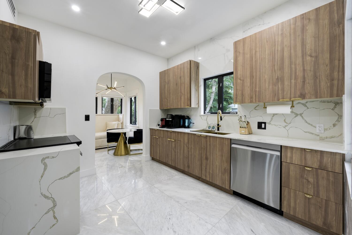 A modern kitchen features wood-grain cabinets, white marble countertops, and stainless steel appliances — 1629 S Lakeside Drive, FL 33460, FL