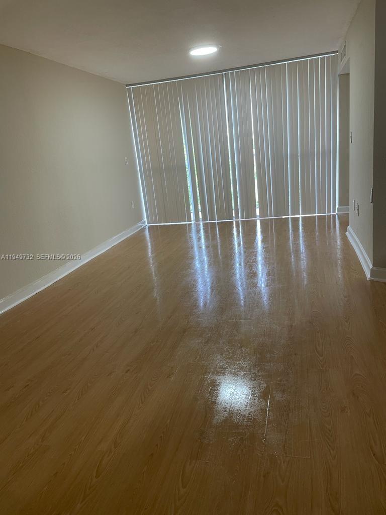 An empty room features light-colored wood-look flooring and vertical blinds covering a large window — 7075 NW 186th St # C505, Hialeah FL 33015, HIALEAH, FL