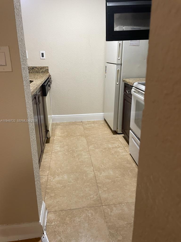 A galley-style kitchen features white appliances, dark wood cabinets, and tan tile flooring — 7075 NW 186th St # C505, Hialeah FL 33015, HIALEAH, FL