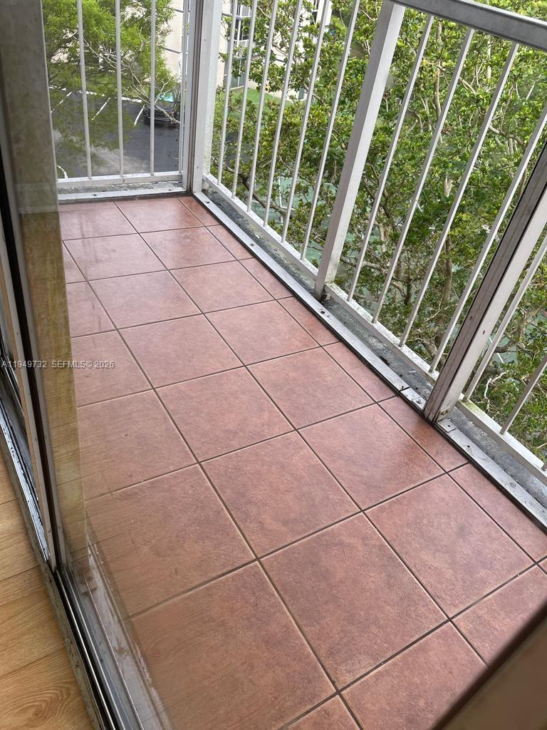 A balcony with brown square floor tiles and white metal railings overlooking trees and parking — 7075 NW 186th St # C505, Hialeah FL 33015, HIALEAH, FL
