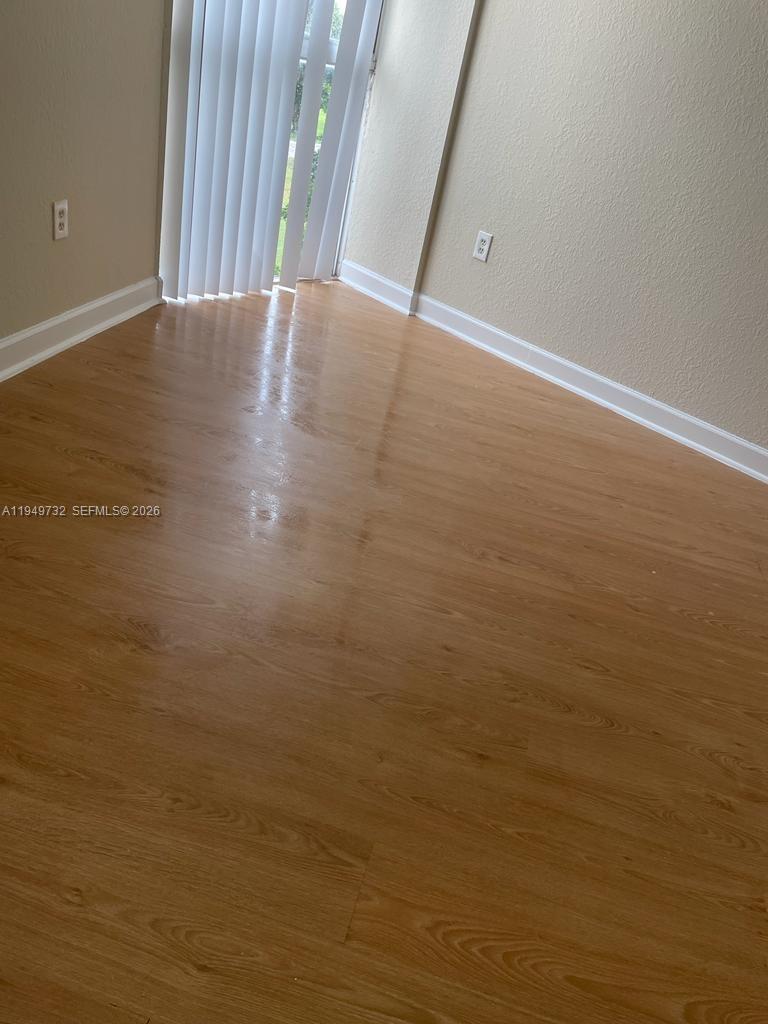 An empty room features light wood-look flooring, beige walls, and vertical blinds over a door — 7075 NW 186th St # C505, Hialeah FL 33015, HIALEAH, FL