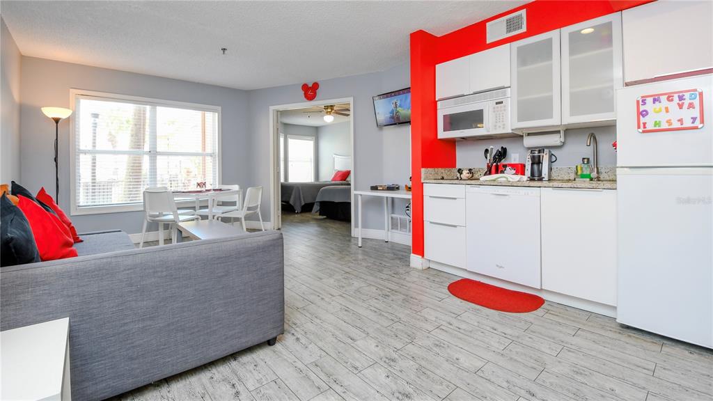 A living room and kitchen area with light wood-look flooring and a red accent wall — 3100 PARKWAY BOULEVARD UNIT 315, KISSIMMEE, FL