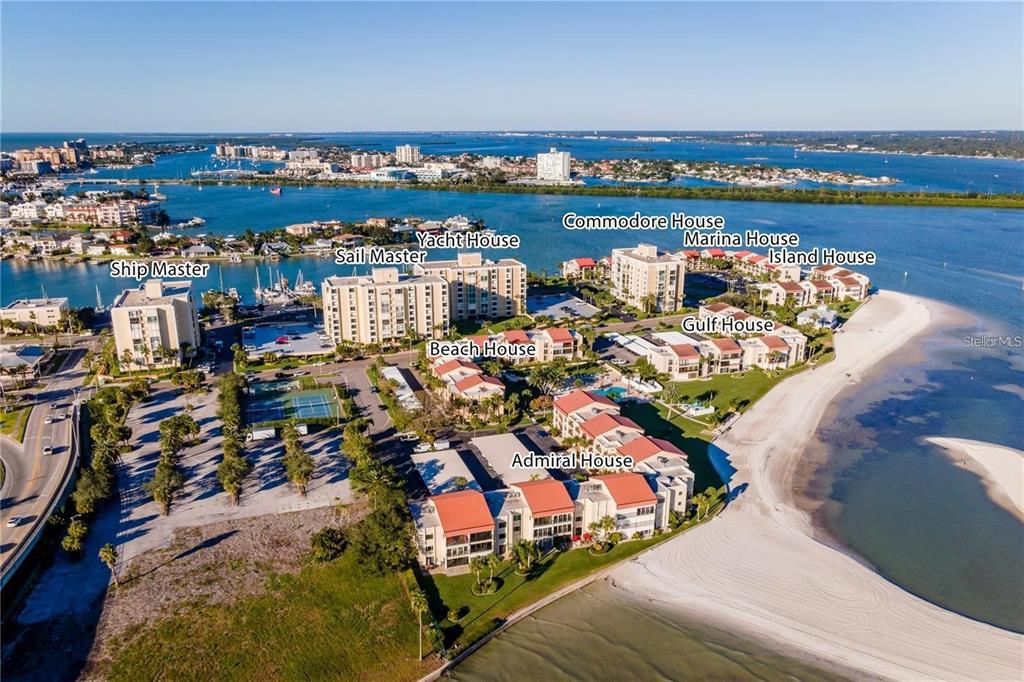 An aerial view shows several multi-story residential buildings situated along a sandy beach and marina — 845 S GULFVIEW BOULEVARD UNIT 110, CLEARWATER BEACH, FL