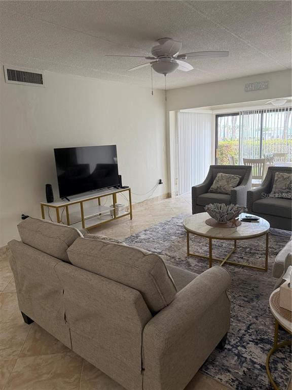 A living room features a sofa, two armchairs, a television on a stand, and tile flooring — 845 S GULFVIEW BOULEVARD UNIT 110, CLEARWATER BEACH, FL