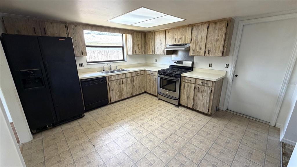 A kitchen features wood-grain cabinets, black appliances, a stainless steel stove, and tiled flooring — 7420 BURNWAY DRIVE, ORLANDO, FL