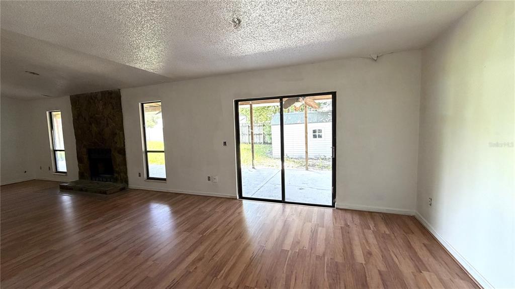 A living room features wood-look flooring, a stone fireplace, and sliding glass doors to a patio — 7420 BURNWAY DRIVE, ORLANDO, FL