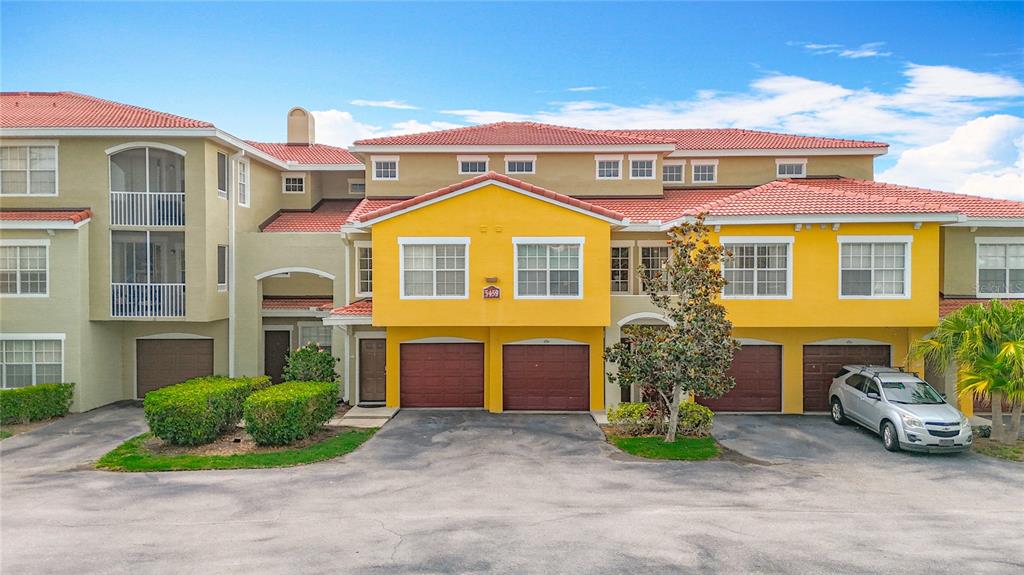 A multi-story townhouse complex features yellow stucco walls, red tile roofs, and several garage doors — 5459 BENTGRASS DRIVE UNIT 2-116, SARASOTA, FL