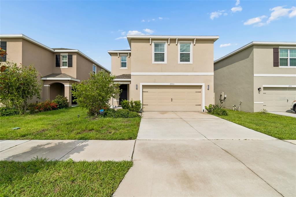 A two-story suburban house with a beige exterior, a two-car garage, and a concrete driveway — 17053 OVAL RUM DRIVE, WIMAUMA, FL