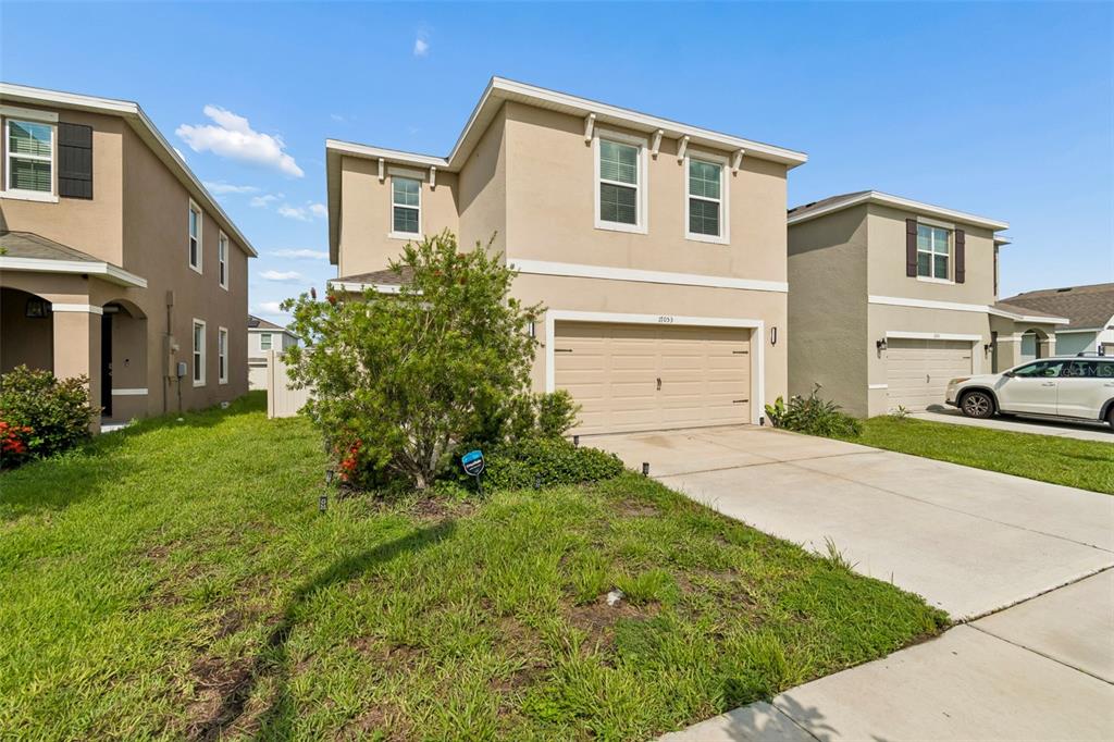 A two-story suburban house with a beige exterior, a two-car garage, and a front lawn — 17053 OVAL RUM DRIVE, WIMAUMA, FL