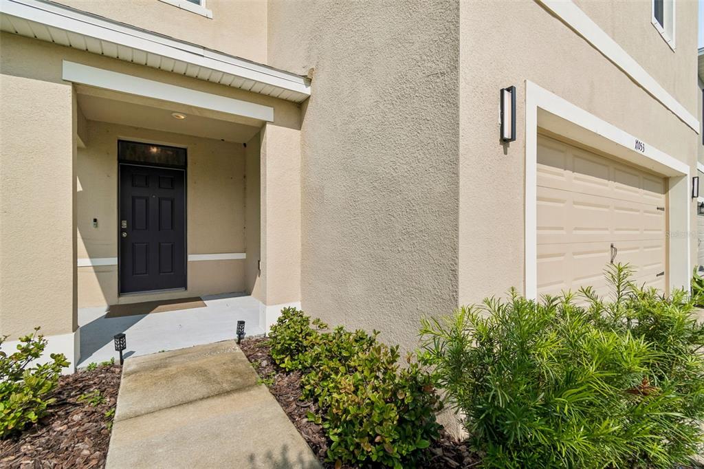 A tan stucco house exterior features a dark front door and a single-car garage — 17053 OVAL RUM DRIVE, WIMAUMA, FL