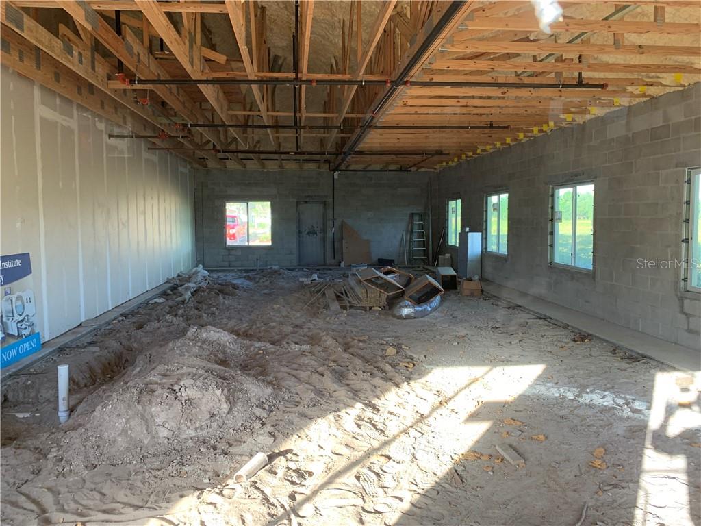 An unfinished commercial interior features exposed wooden roof trusses, concrete block walls, and a dirt floor — 5140 DEER PARK DRIVE, NEW PORT RICHEY, FL