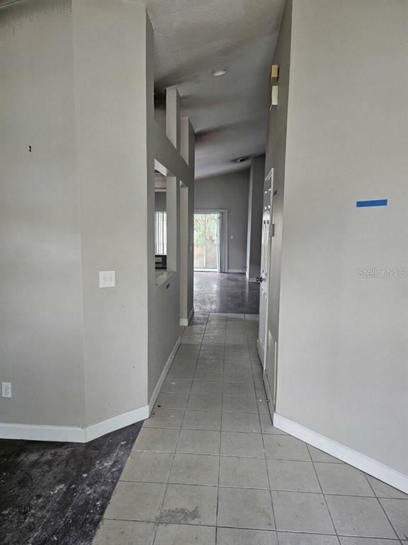 A hallway with light-colored tile flooring leads toward a doorway with a view outside — 1929 SEDGEFIELD STREET, BRANDON, FL
