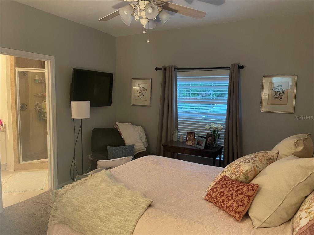A bedroom with wood-look flooring, a ceiling fan, a wall-mounted television, and an attached bathroom — 4945 NW 1ST PLACE, GAINESVILLE, FL