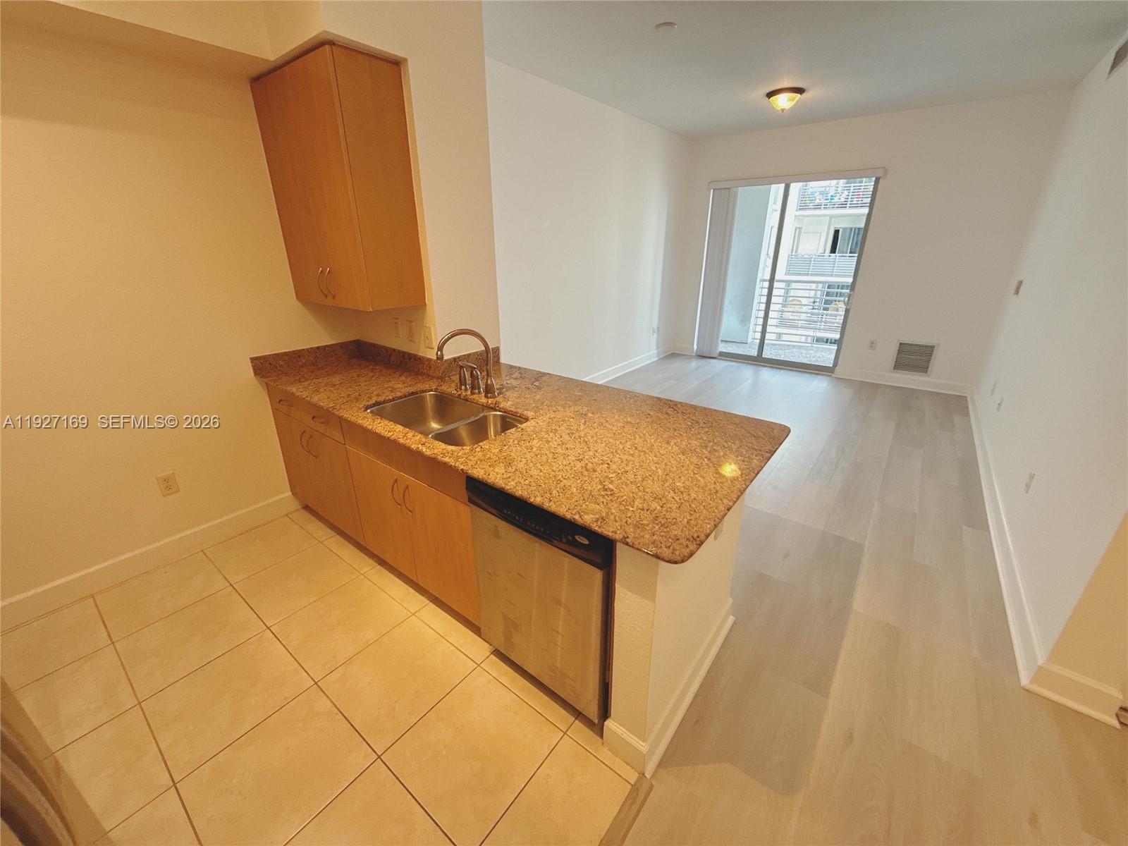 A kitchen with granite countertops and light wood cabinets overlooks an open living area — 1830 Radius Dr # 1121, Hollywood FL 33020, HOLLYWOOD, FL