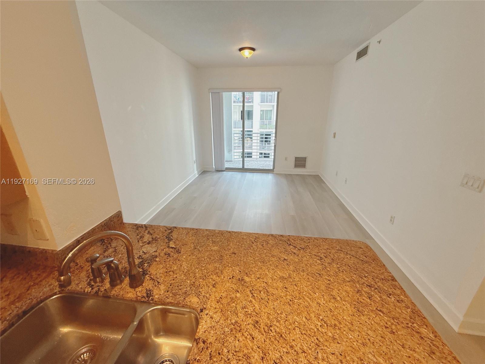 A kitchen sink with granite countertops overlooks an empty living area with light wood flooring — 1830 Radius Dr # 1121, Hollywood FL 33020, HOLLYWOOD, FL