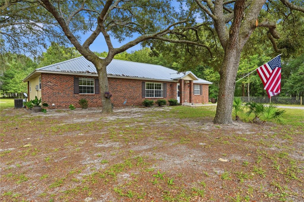 A single-story brick house with a metal roof sits on a grassy lot with trees — 5480 NE 53RD TERRACE, HIGH SPRINGS, FL