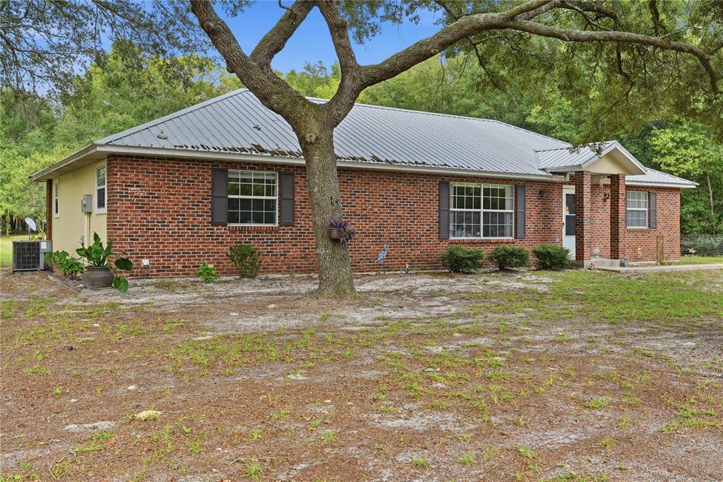 A single-story brick house with a metal roof sits on a sandy lot with trees — 5480 NE 53RD TERRACE, HIGH SPRINGS, FL