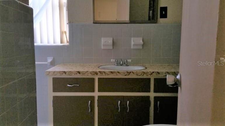 A bathroom vanity with a patterned countertop, dark cabinets, and a tiled backsplash — 608 LEMON STREET, AUBURNDALE, FL