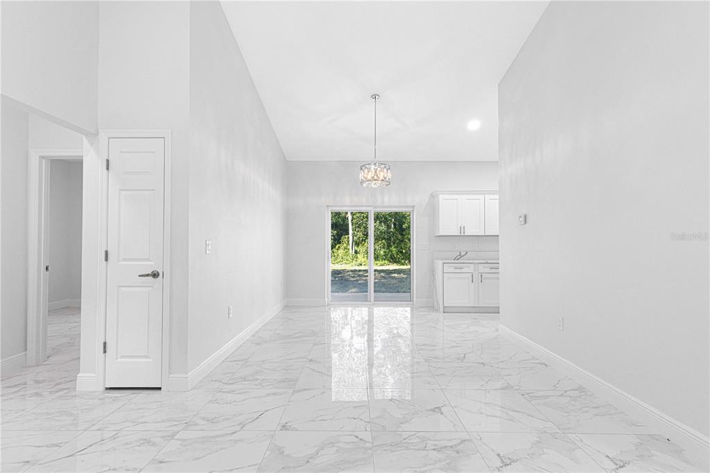 A bright dining area features white marble-look tile flooring, a crystal chandelier, and sliding glass doors — 15223 SE 61ST COURT, SUMMERFIELD, FL