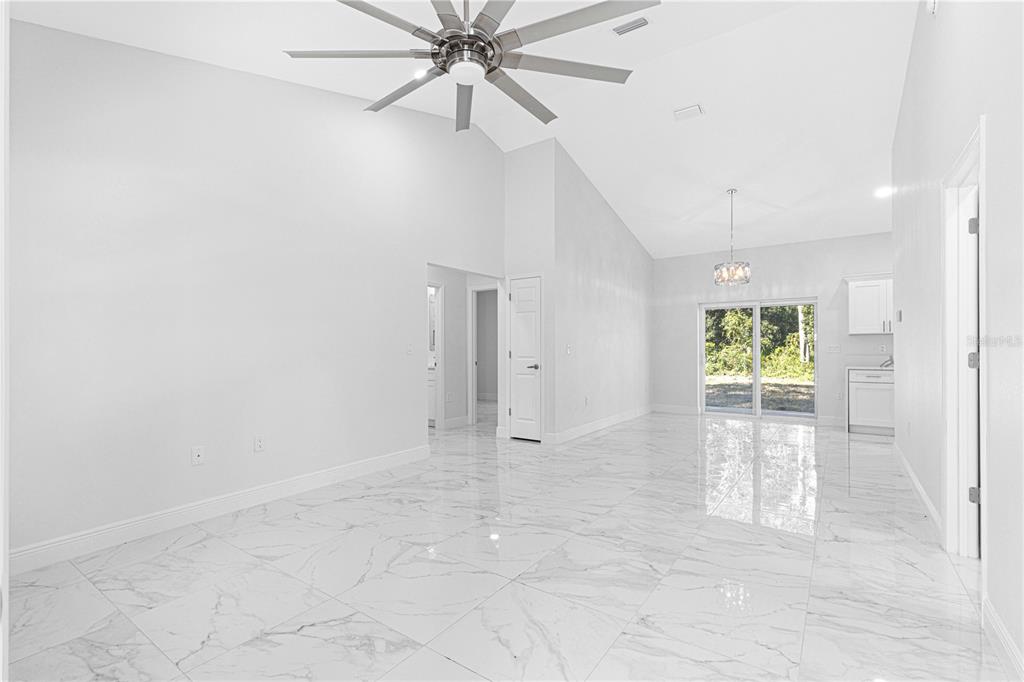 A bright, open-concept living area features white marble-look tile flooring and a vaulted ceiling — 15223 SE 61ST COURT, SUMMERFIELD, FL