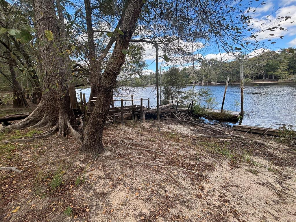 A sandy riverbank features a weathered wooden dock extending into the water under large trees — 1347 NE 519TH AVENUE, OLD TOWN, FL