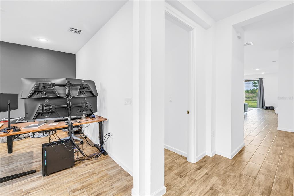 A home office with a multi-monitor desk setup sits beside a hallway leading to a living area — 11332 GALLATIN TRAIL, PARRISH, FL