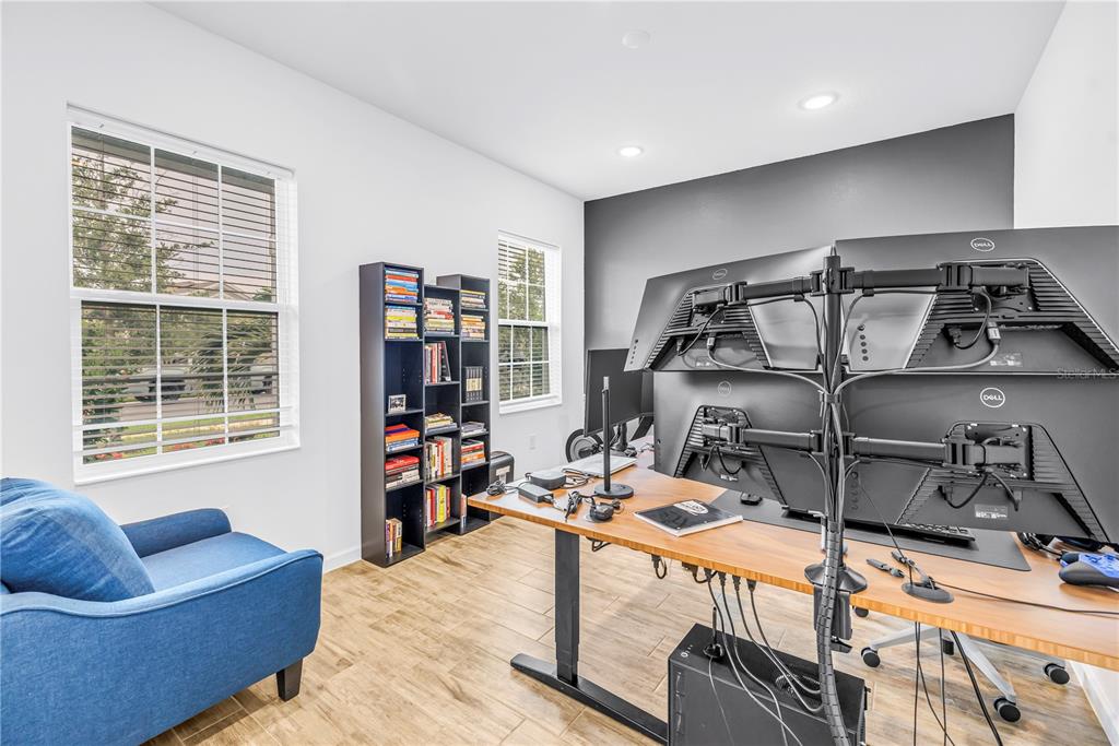A home office features a wood-topped standing desk, multiple monitors, a bookshelf, and a blue chair — 11332 GALLATIN TRAIL, PARRISH, FL