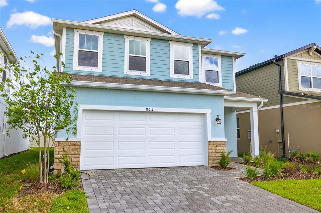 A two-story house with light blue siding, a white garage door, and a paver driveway — 13014 SUNSEED STREET, PARRISH, FL