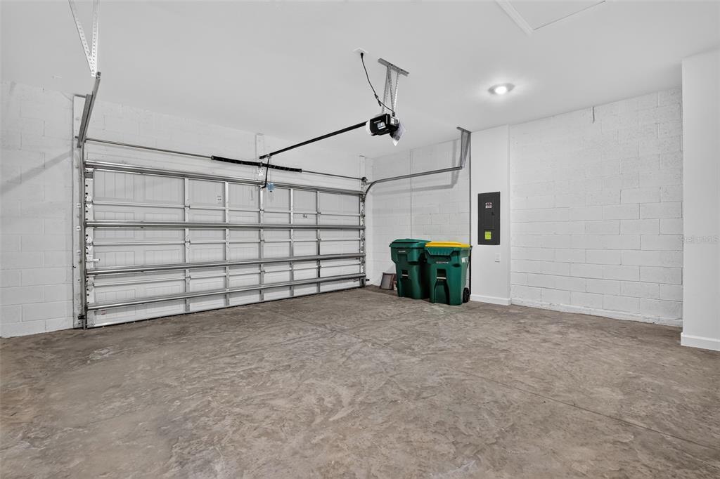 An empty garage with a concrete floor, white block walls, and two green trash bins — 26627 WILGROVE PLACE, PUNTA GORDA, FL