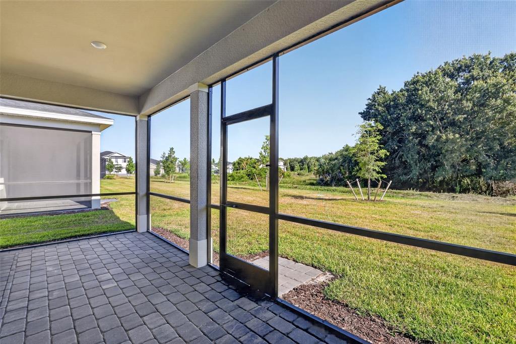 A screened-in patio with paver flooring overlooks a grassy backyard and a line of trees — 26627 WILGROVE PLACE, PUNTA GORDA, FL