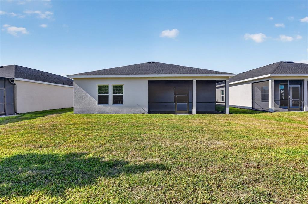 The rear exterior of a single-story house features a screened-in lanai and a grassy yard — 26627 WILGROVE PLACE, PUNTA GORDA, FL